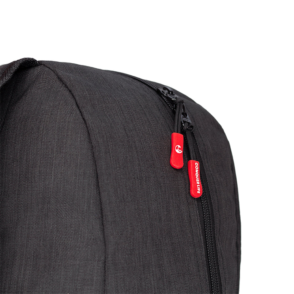 Closeup side view of black poly-fabric backpack, black plastic zipper and red rubber pulls